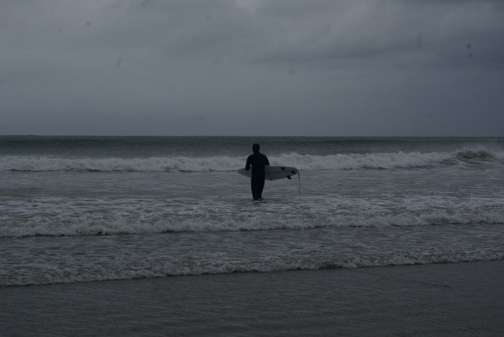 Decathlond Shortboard 900 im Test: Ein Mann im Neo mit Haube blickt aufs Meer